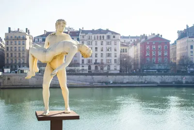 A photograph of the statue 'The Weight of Oneself' in Lyon, France, featuring a standing man carrying another man, limp as if near death, yet both are identical, representing the same man.